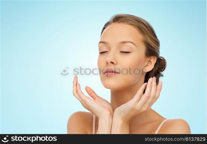 beauty, people, skincare and health concept - young woman face and hands over blue background