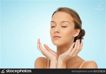 beauty, people, skincare and health concept - young woman face and hands over blue background