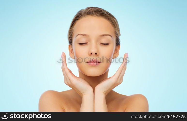 beauty, people, skincare and health concept - young woman face and hands over blue background