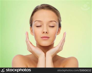 beauty, people, skincare and health concept - young woman face and hands over green background