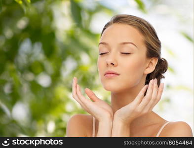 beauty, people, skincare and health concept - young woman face and hands over green natural background