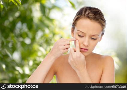 beauty, people, skincare and health concept - young woman squeezing pimple on her face over green natural background