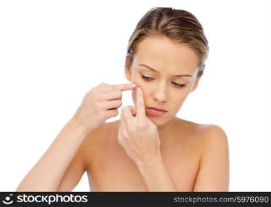 beauty, people, skincare and health concept - young woman squeezing pimple on her face