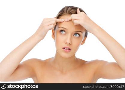 beauty, people, skincare and health concept - young woman squeezing pimple on her face