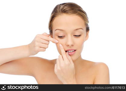 beauty, people, skincare and health concept - young woman squeezing pimple on her face