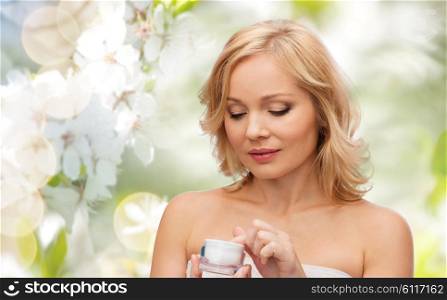 beauty, people, skincare and natural cosmetics concept - middle aged woman with cream jar over cherry blossom background