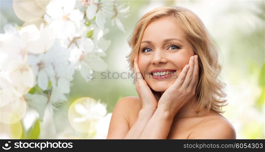 beauty, people, skincare and natural cosmetics concept - smiling woman with bare shoulders touching face over cherry blossom background