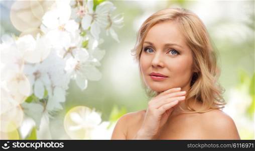 beauty, people, skincare and natural cosmetics concept - woman with bare shoulders touching face over cherry blossom background