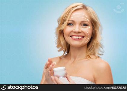 beauty, people, skincare, anti-aging and cosmetics concept - happy woman with cream jar over blue background