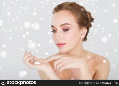 beauty, people, skincare, winter and cosmetics concept - happy young woman with moisturizing cream on hand over gray background and snow