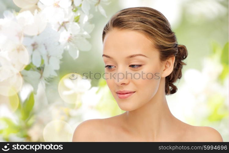 beauty, people, spring, nature and health concept - smiling young woman face and shoulders over cherry blossom background