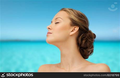 beauty, people, summer, skincare and health concept - young woman face with closed eyes sunbathing side view over blue sea and sky background