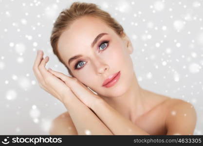 beauty, people, winter and bodycare concept - beautiful young woman face and hands over gray background and snow