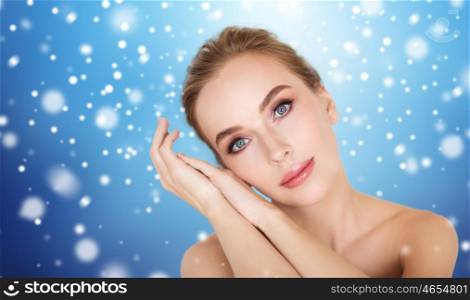 beauty, people, winter and bodycare concept - beautiful young woman face and hands over blue background and snow