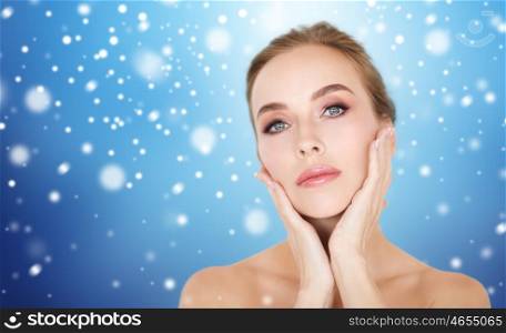 beauty, people, winter and bodycare concept - beautiful young woman face and hands over blue background and snow