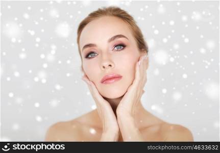 beauty, people, winter and bodycare concept -beautiful young woman face and hands over gray background and snow