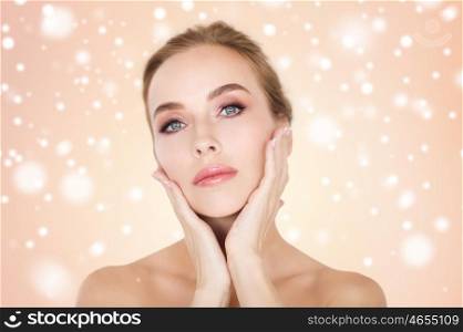 beauty, people, winter and bodycare concept -beautiful young woman face and hands over beige background and snow
