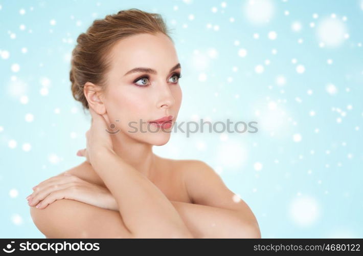 beauty, people, winter and bodycare concept -beautiful young woman face and hands over blue background and snow