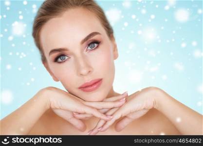 beauty, people, winter and bodycare concept - close up of beautiful young woman face and hands over blue background and snow