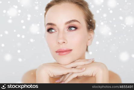 beauty, people, winter and bodycare concept - close up of beautiful young woman face and hands over gray background and snow