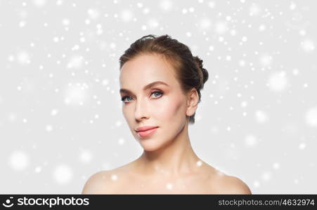 beauty, people, winter and health concept - beautiful young woman face over gray background and snow