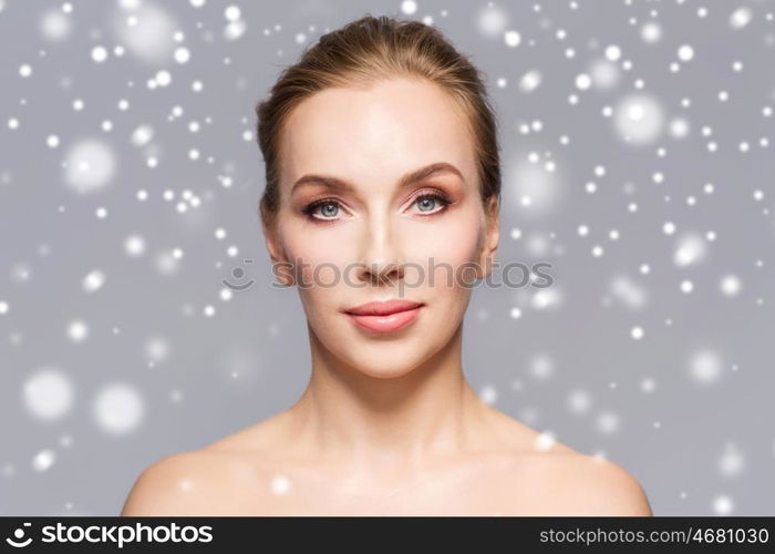 beauty, people, winter and health concept - beautiful young woman face over gray background and snow