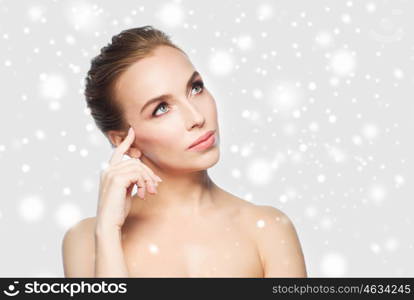 beauty, people, winter and health concept - beautiful young woman touching her face over gray background and snow