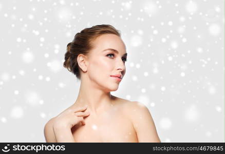 beauty, people, winter and health concept - beautiful young woman touching her neck over gray background and snow