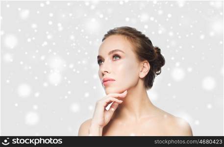 beauty, people, winter and health concept - beautiful young woman touching her face over gray background and snow