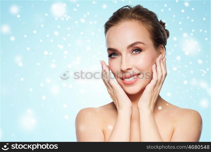 beauty, people, winter and health concept - beautiful young woman touching her face over blue background and snow