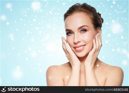 beauty, people, winter and health concept - beautiful young woman touching her face over blue background and snow