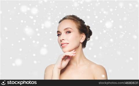 beauty, people, winter and health concept - beautiful young woman touching her face over gray background and snow