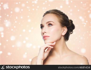 beauty, people, winter and health concept - beautiful young woman touching her face over beige background and snow