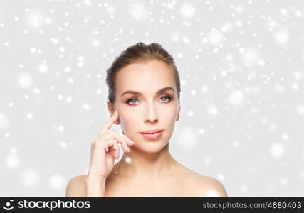 beauty, people, winter and plastic surgery concept - beautiful young woman showing her cheekbone over gray background and snow