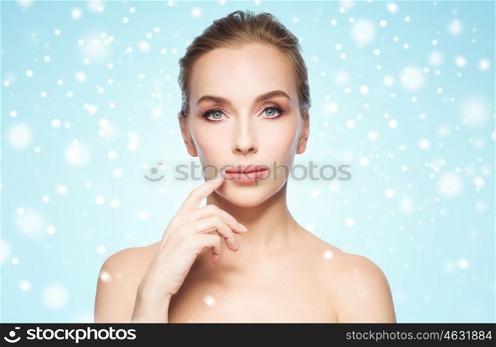 beauty, people, winter, health and plastic surgery concept - beautiful young woman showing her lips over blue background and snow