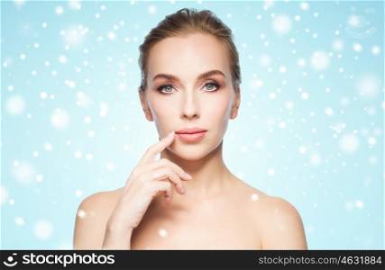 beauty, people, winter, health and plastic surgery concept - beautiful young woman showing her lips over blue background and snow