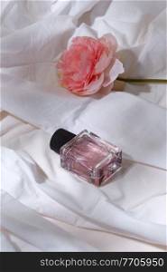 beauty, perfumery and object concept - bottle of perfume and flower on white sheet with folds. bottle of perfume and flower on white sheet