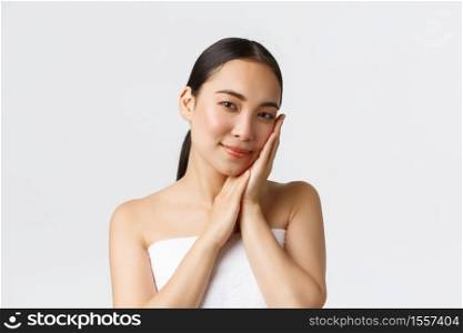 Beauty, personal care, spa salon and skincare concept. Tender beautiful asian girl in bath towel gently touching her cheek, satisfied with skin condition, got rid of acne, smiling delighted.. Beauty, personal care, spa salon and skincare concept. Tender beautiful asian girl in bath towel gently touching her cheek, satisfied with skin condition, got rid of acne, smiling delighted