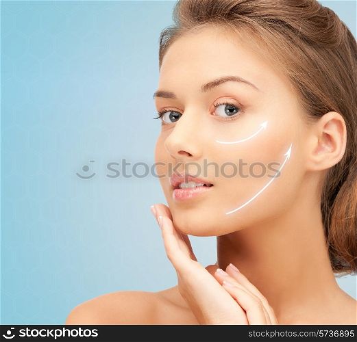 beauty, plastic surgery, aging, people and health concept - beautiful young woman touching her face with lifting arrows over blue background