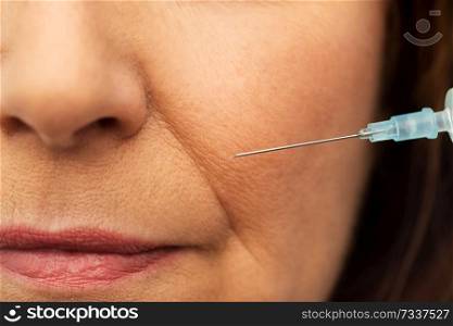 beauty, plastic surgery and cosmetology concept - close up of senior woman face and syringe. close up of senior woman face and syringe
