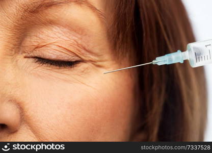 beauty, plastic surgery and cosmetology concept - close up of senior woman face and syringe. close up of senior woman face and syringe