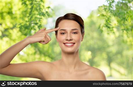 beauty, plastic surgery and people concept - beautiful young woman with bare shoulders showing her forehead over green natural background. beautiful young woman showing her forehead