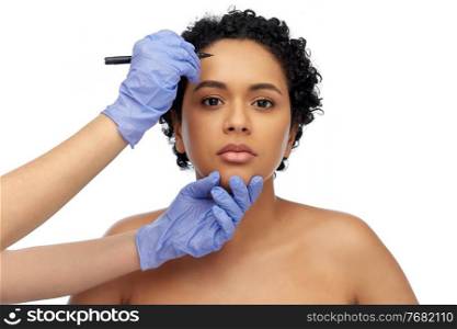 beauty, plastic surgery and people concept - close up of face of beautiful young african american woman and hands in gloves with marker over white background. face of african woman and hands with marker