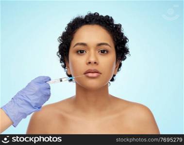 beauty, plastic surgery and people concept - close up of face of beautiful young african american woman and hand with syringe over blue background. face of african woman and hand with syringe