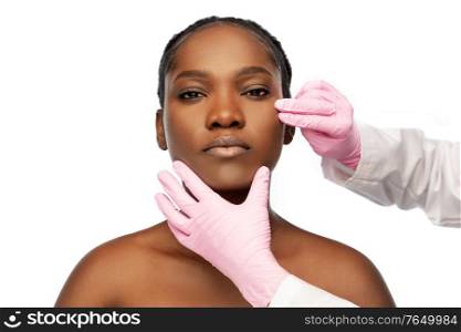 beauty, plastic surgery and people concept - portrait of beautiful young african american woman and hands in medical gloves over white background. african american woman and hands in medical gloves