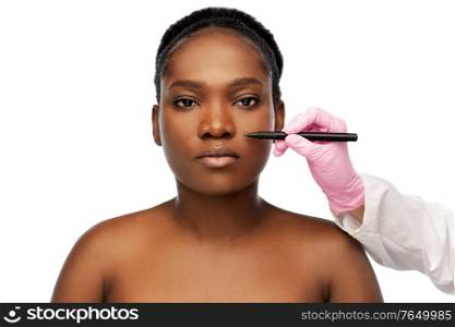 beauty, plastic surgery and people concept - portrait of beautiful young african american woman and hand in glove with marker over white background. face of african woman and hand with marker