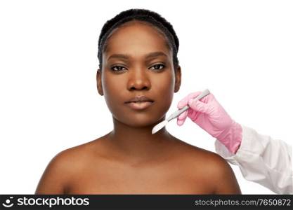 beauty, plastic surgery and people concept - portrait of beautiful young african american woman and hand with scalpel knife over white background. face of african american woman and scalpel knife