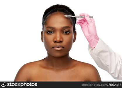 beauty, plastic surgery and people concept - portrait of beautiful young african american woman and hand with scalpel knife over white background. face of african american woman and scalpel knife