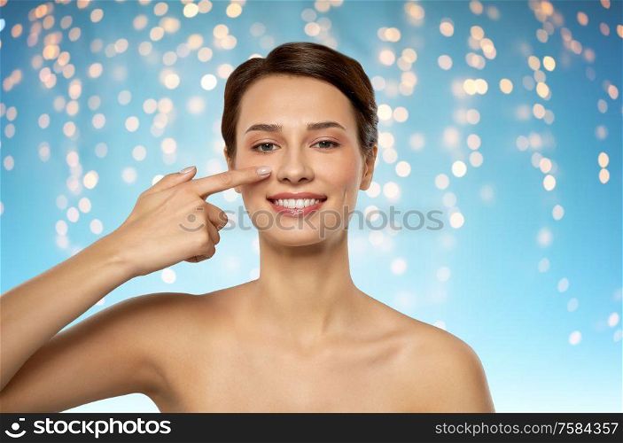 beauty, plastic surgery and people concept - smiling beautiful young woman showing her nose over holidays lights on blue background. beautiful smiling woman showing her nose