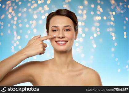 beauty, plastic surgery and people concept - smiling beautiful young woman showing her nose over holidays lights on blue background. beautiful smiling woman showing her nose